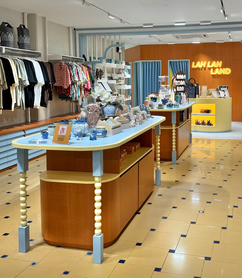 Lah Lah Land's retail store interior at Petaling Street with clothing racks lining both sides, display tables in the foreground, and a branded yellow signage reading 'LAH LAH LAND'. No single apparel item is isolated as the product; the scene shows the store layout and fixtures.